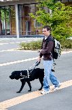 Guide Dog trialist walking and using hand controller to find signal from a base station.